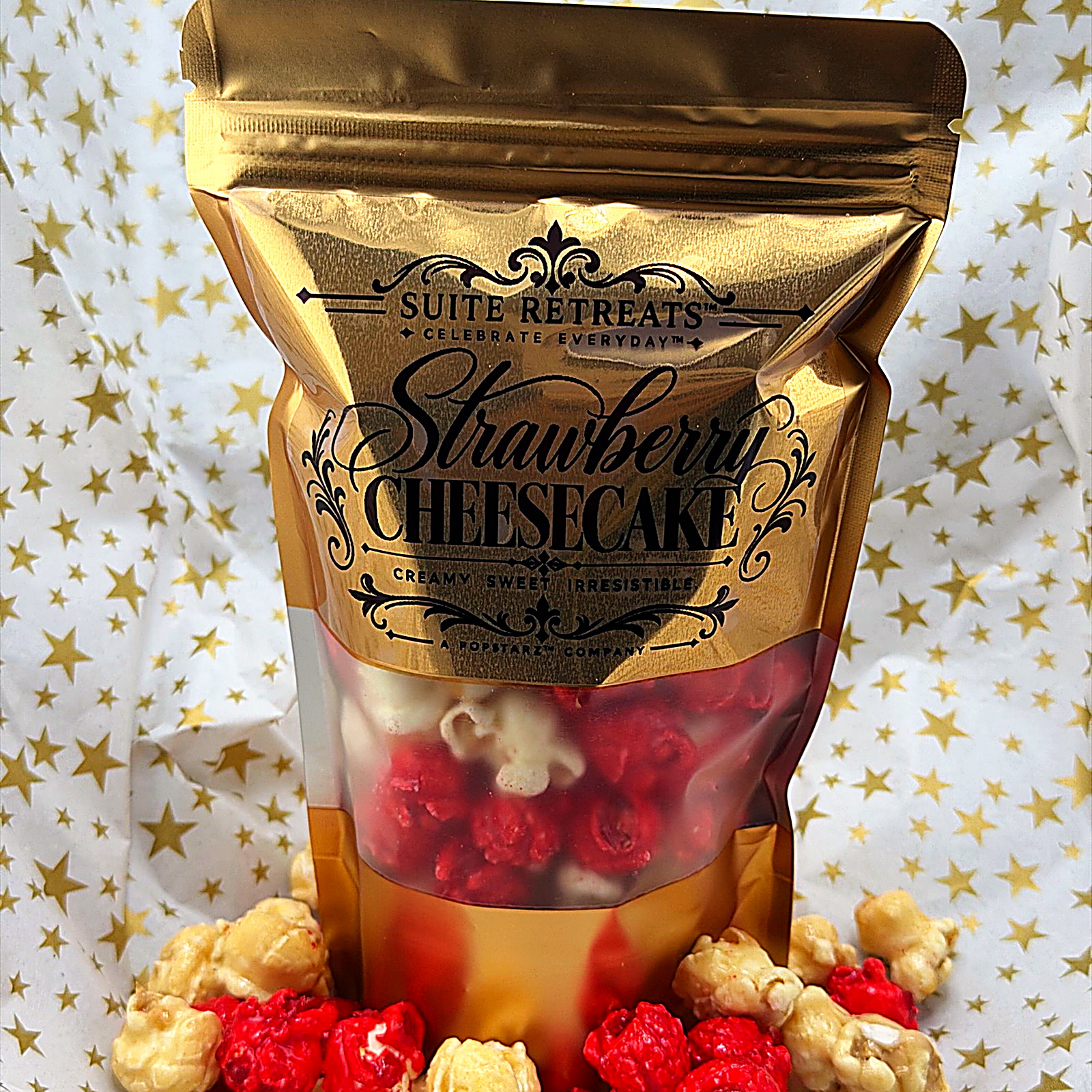 A gold Suite Retreats Strawberry Cheesecake pouch on gold-star tissue, pink and caramel popcorn at its base