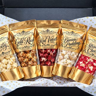 All five Suite Retreats gold pouches — Levity, Gold Rush, Red Velvet, Banana Pudding and Strawberry Cheesecake — fanned inside the open black gift box on gold-star tissue