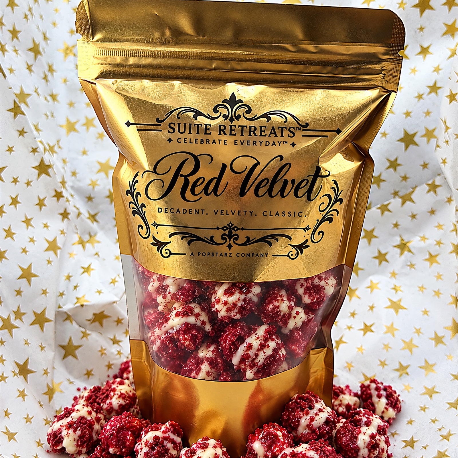 A gold Suite Retreats Red Velvet pouch of red velvet popcorn with white chocolate drizzle, on gold-star tissue