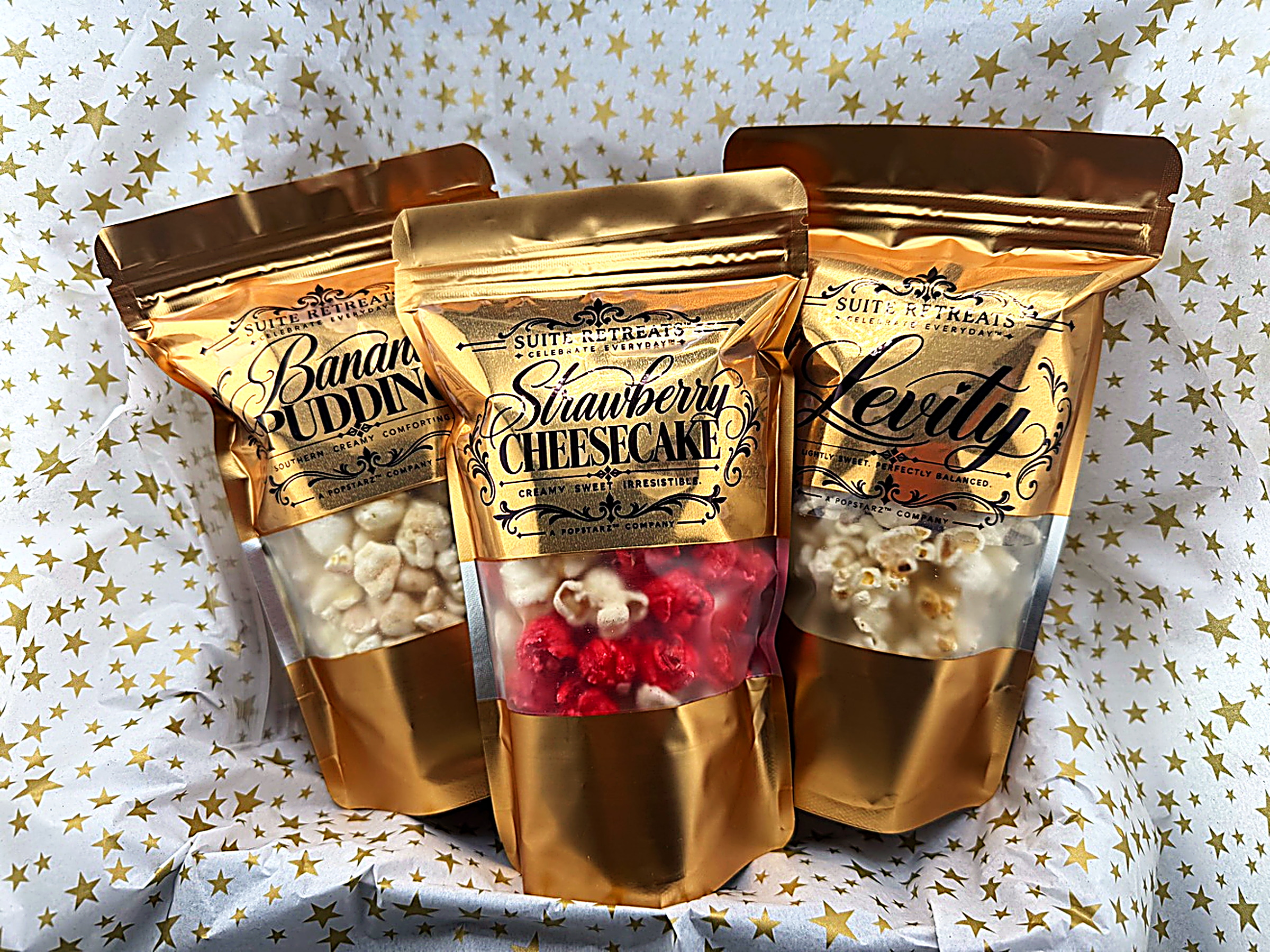 Three gold Suite Retreats pouches — Banana Pudding, Strawberry Cheesecake and Levity — fanned out on gold-star tissue